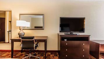 A hotel room with a desk, chair, television, and a dresser.