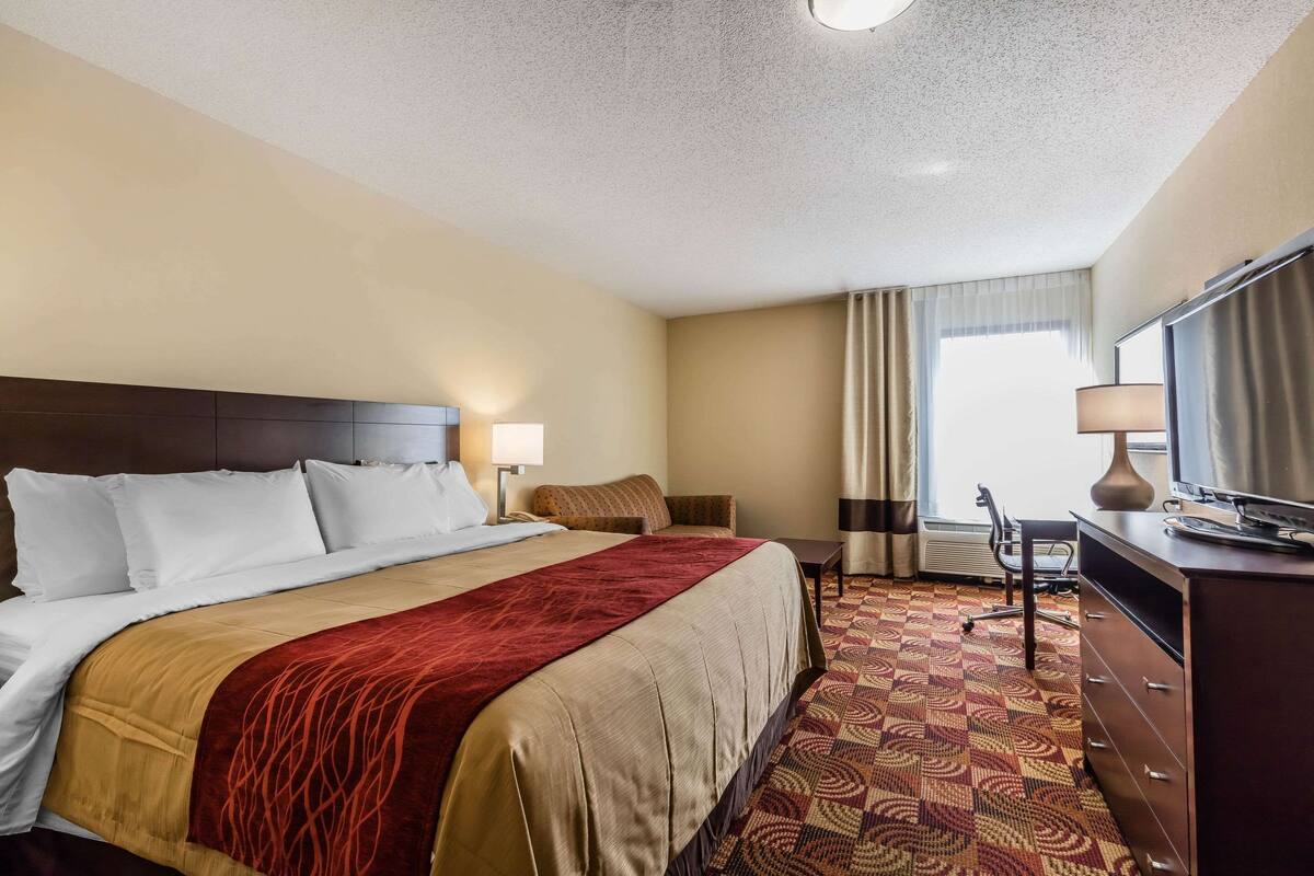 A hotel room with a large bed, a desk, a chair, and a television.