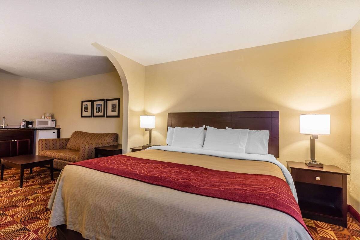 A hotel room with a large bed, two bedside lamps, a desk with a chair, and a microwave.