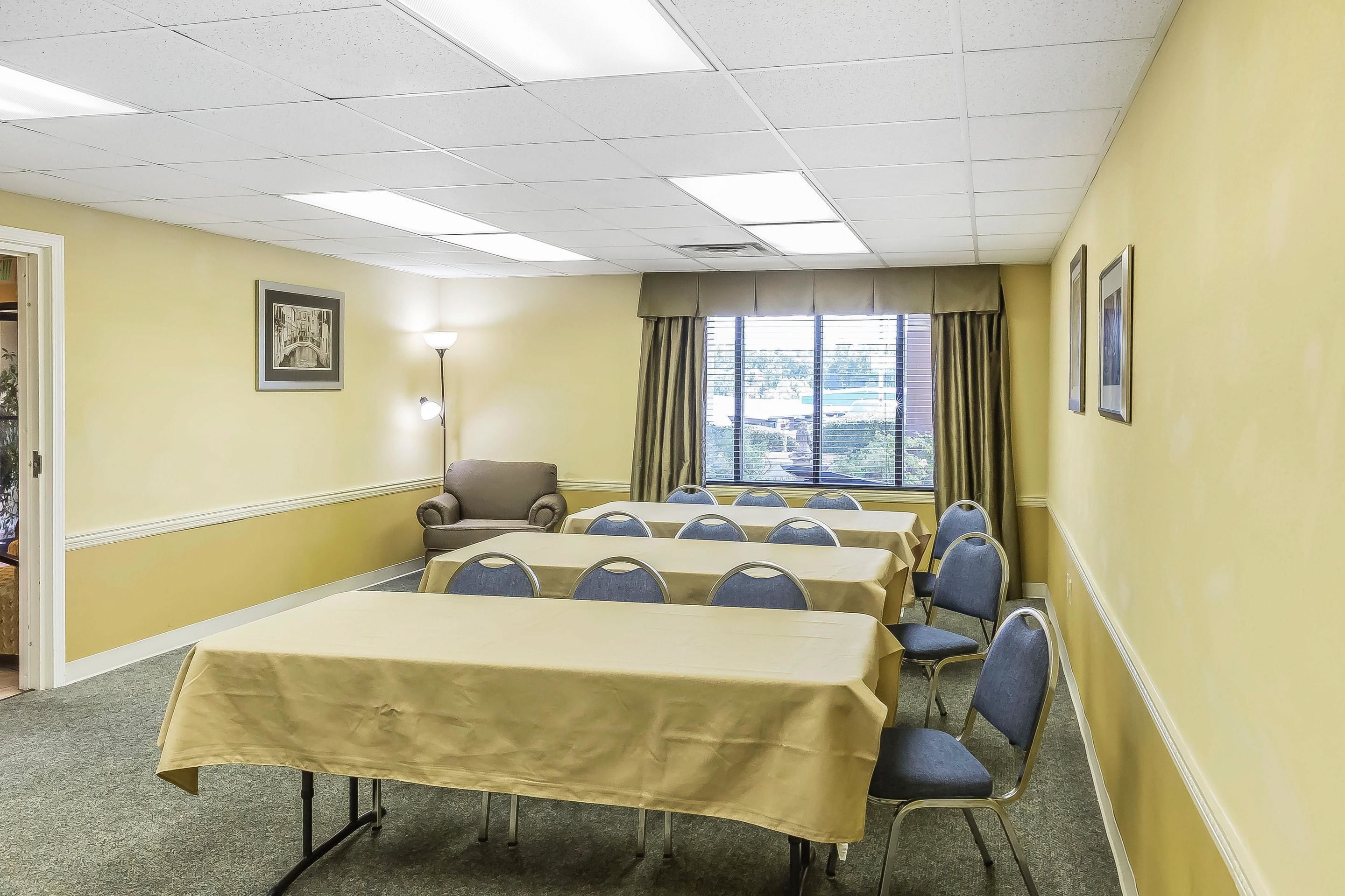 A conference room with tables and chairs, a window with curtains, and a framed picture on the wall.