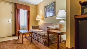 A hotel room with a sofa, a small table, a lamp, and a painting on the wall. - Quality Inn Calera I-65 exit 231 (Calera)