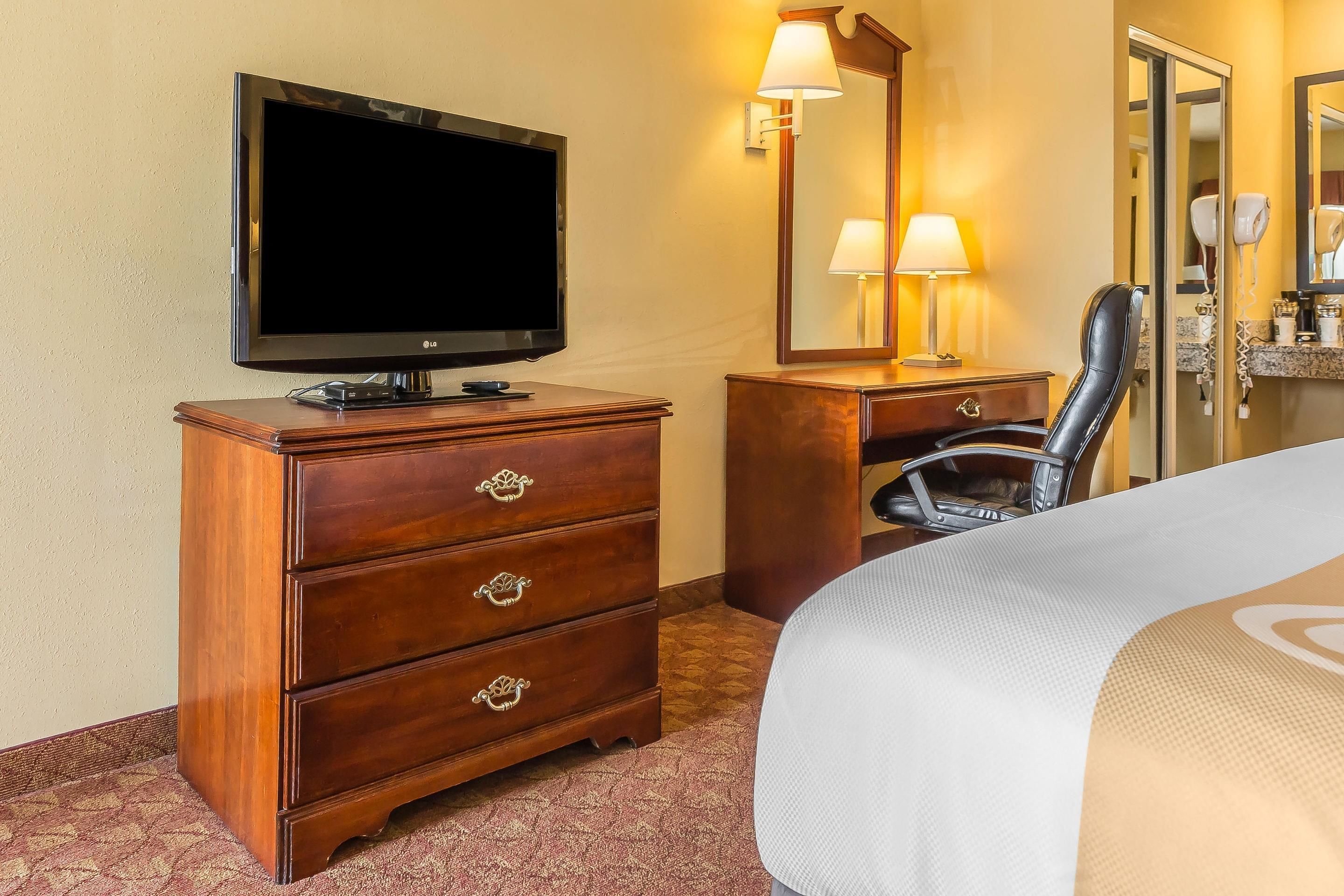 Ein Hotelzimmer mit Fernseher, einem Holzschrank, einem Sessel und einem Bett.