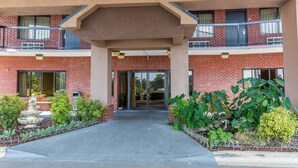 A brick building with a covered entrance, a small fountain, and a garden with various plants. - Quality Inn Calera I-65 exit 231 (Calera)