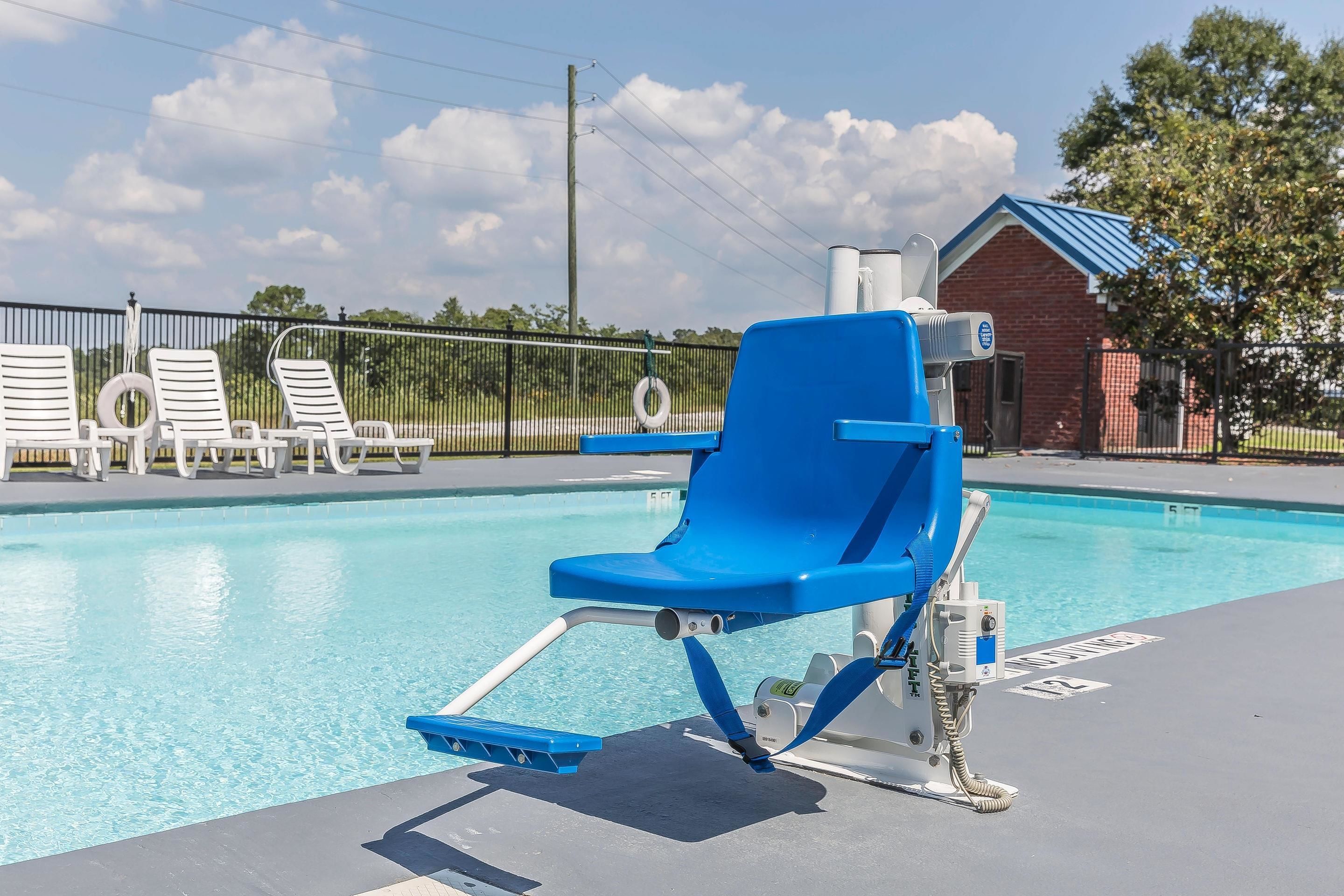 A poolside area with a blue lounge chair, white lounge chairs, and a brick building in the background.