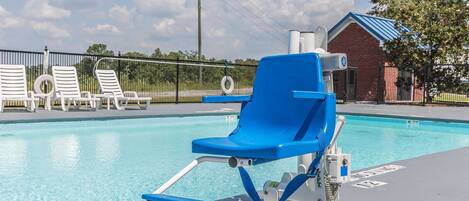 A poolside area with a blue lounge chair, white lounge chairs, and a brick building in the background.