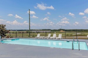 A swimming pool with white lounge chairs and a metal fence.