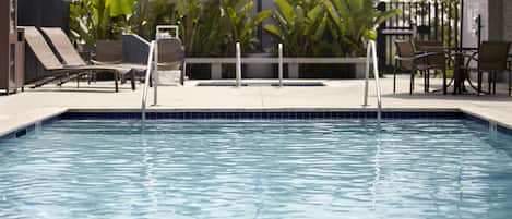 A swimming pool with lounge chairs and a table, surrounded by tropical plants.