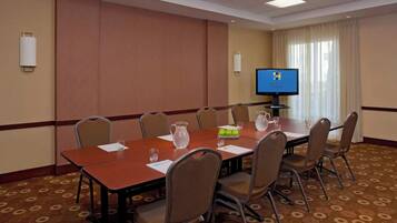 A conference room with a long table, chairs, a television screen, and a window with curtains.