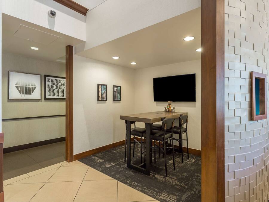 A hotel room with a dining area featuring a table and chairs, a flat-screen TV mounted on the wall, and framed artwork on the wall.