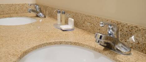 A bathroom with two sinks and faucets, a mirror, and toiletries on the countertop.