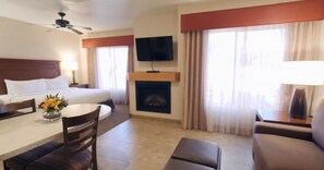 A hotel room with a bed, a TV mounted on the wall, a fireplace, a dining area with a table and chairs, and a sofa.