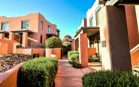 A hotel corridor with a clear view of a mountain in the distance, featuring modern architecture with a reddish-brown facade and a paved walkway.