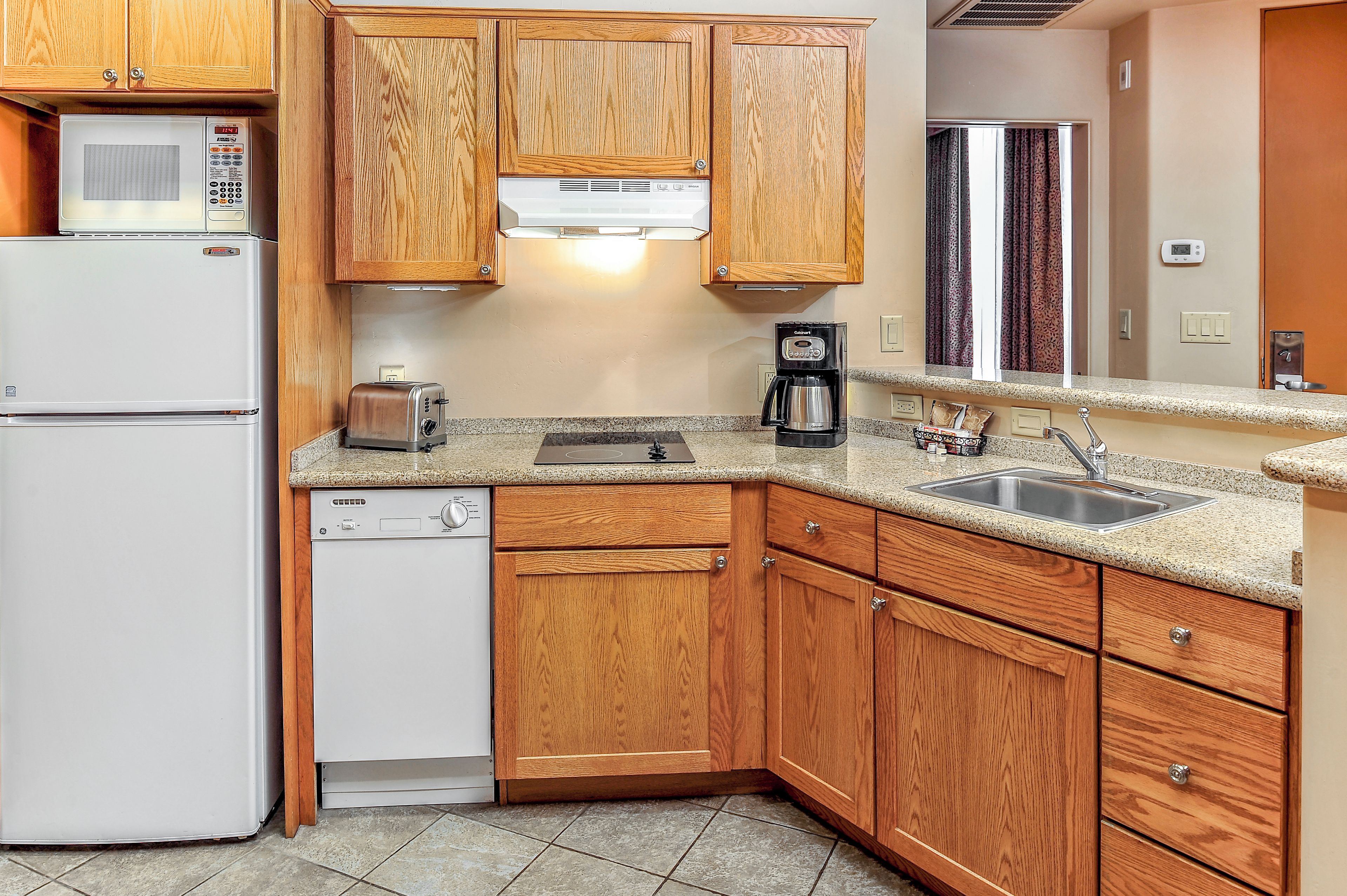 A compact kitchen with wooden cabinets, a microwave, a toaster, a coffee maker, and a dishwasher.