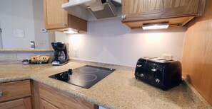 A kitchen with wooden cabinets, a black induction cooktop, a toaster, and a coffee maker.