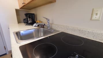 A kitchen with a stainless steel sink, a black induction cooktop, a coffee maker, and a small cabinet above the sink.