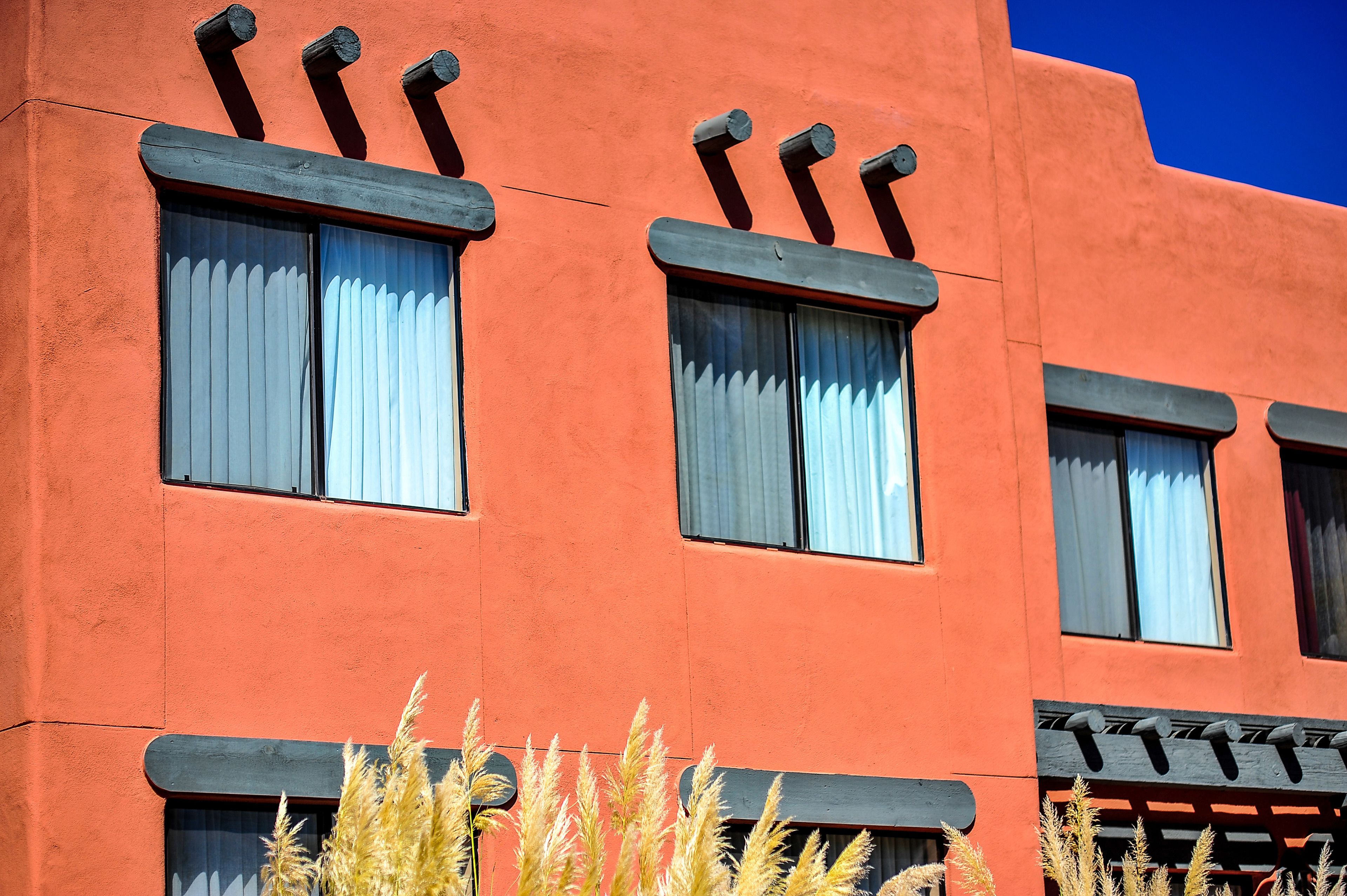 Un edificio con fachada roja, varias ventanas con cortinas blancas y un toldo negro.