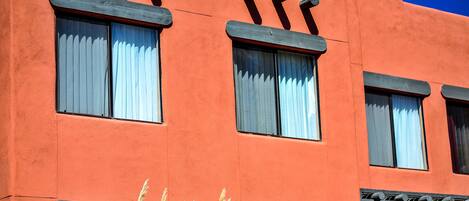 Un edificio con fachada roja, varias ventanas con cortinas blancas y un toldo negro.