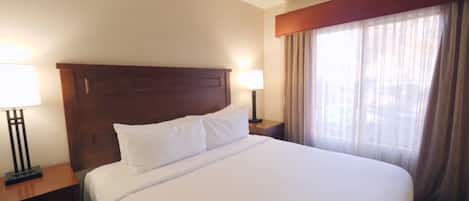 Hotelkamer met een groot bed, houten hoofdeinde, twee nachtkastjes met lampen en een groot raam met gordijnen.