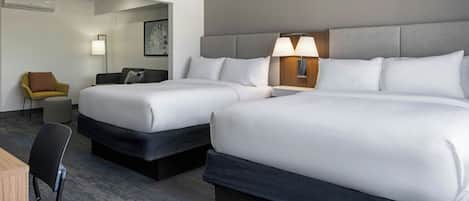 A hotel room with two beds, a desk, a chair, and a lamp.