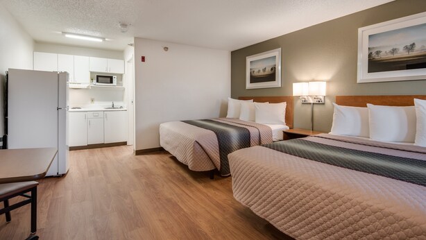 Habitación de hotel con dos camas, kitchenette y zona de comedor.