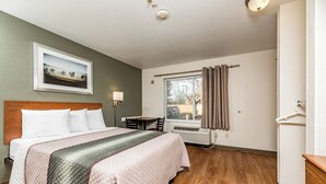 Una habitación de hotel con cama, escritorio, silla, ventana con cortinas y un calentador de pared.