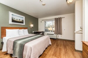 Una habitación de hotel con cama, escritorio, silla, ventana con cortinas y un calentador de pared.