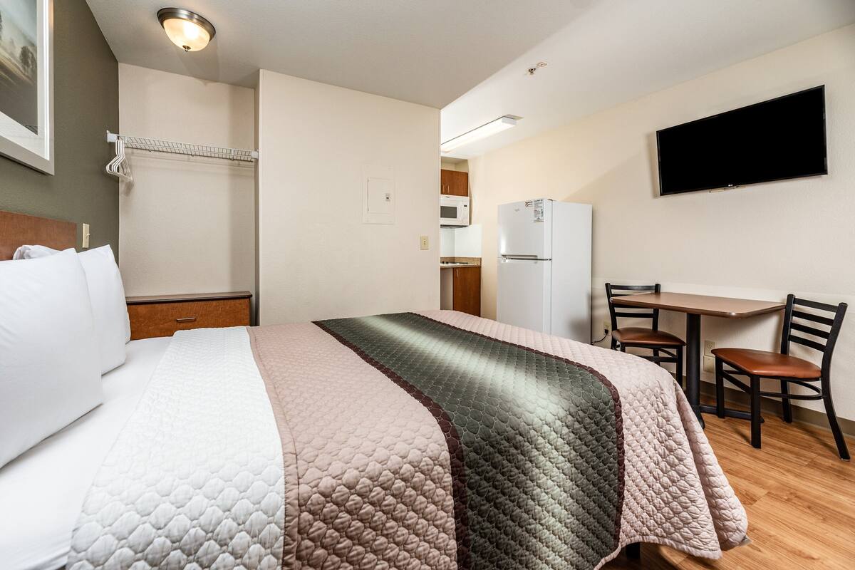 Une chambre d’hôtel équipée d’un lit, d’un bureau, d’une chaise, d’une télévision, d’un réfrigérateur et d’un four à micro-ondes.