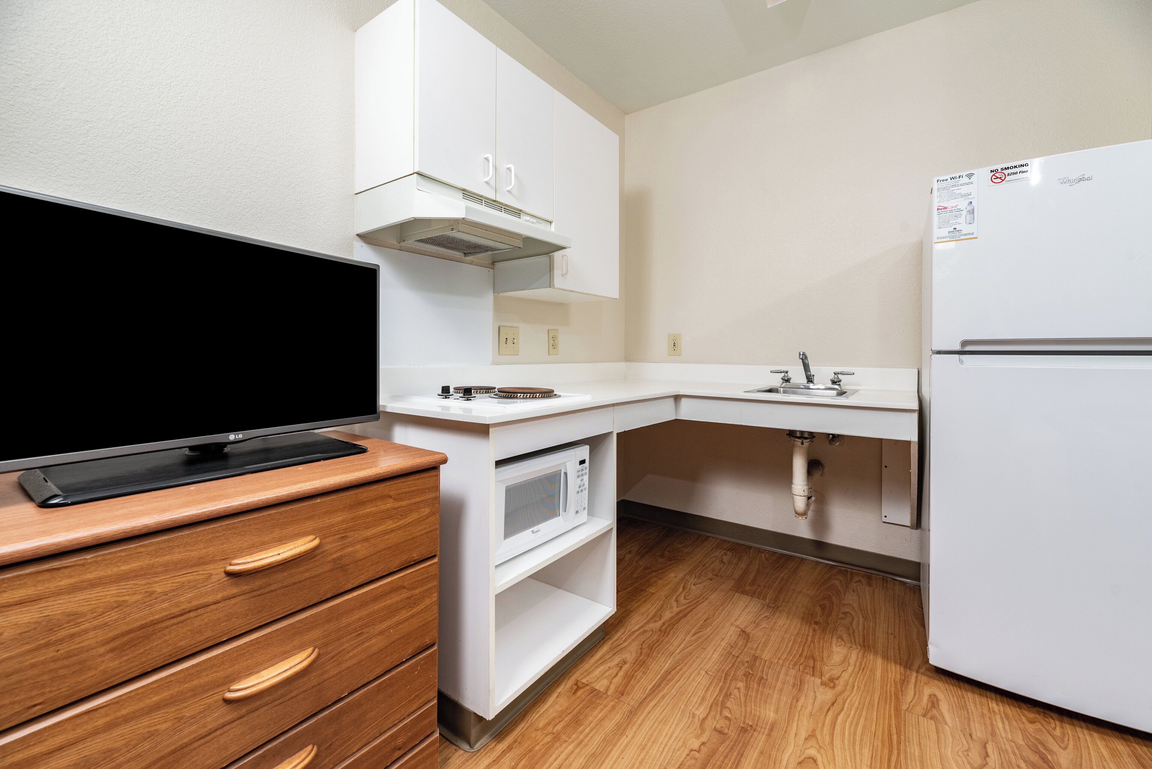Eine kompakte Küchenzeile mit Flachbildfernseher, Mikrowelle, Kühlschrank und Holzschrank.