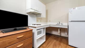 Eine kompakte Küchenzeile mit Flachbildfernseher, Mikrowelle, Kühlschrank und Holzschrank.