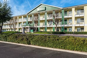 A multi-story hotel with a green and yellow facade, multiple balconies, and a parking area in front. - HomeTowne Studios by Red Roof Fresno - West (Fresno)