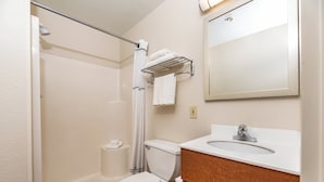 A bathroom with a shower, toilet, sink, and mirror. - HomeTowne Studios by Red Roof Fresno - West (Fresno)