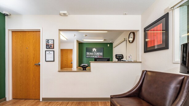Un área de recepción con puerta de madera, mostrador de recepción, un reloj y un sofá de cuero marrón.