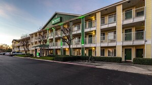 Un hotel de varios pisos con fachada verde y blanca, balcones y un estacionamiento.