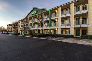Ett hotell med flera våningar, en grön och vit fasad, balkonger och en parkeringsplats.