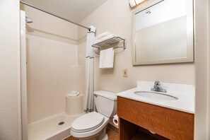 A bathroom with a shower, toilet, sink, and a mirror. - HomeTowne Studios by Red Roof Fresno - West (Fresno)