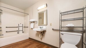 A bathroom with a bathtub, a sink, a toilet, and a mirror. - HomeTowne Studios by Red Roof Fresno - West (Fresno)