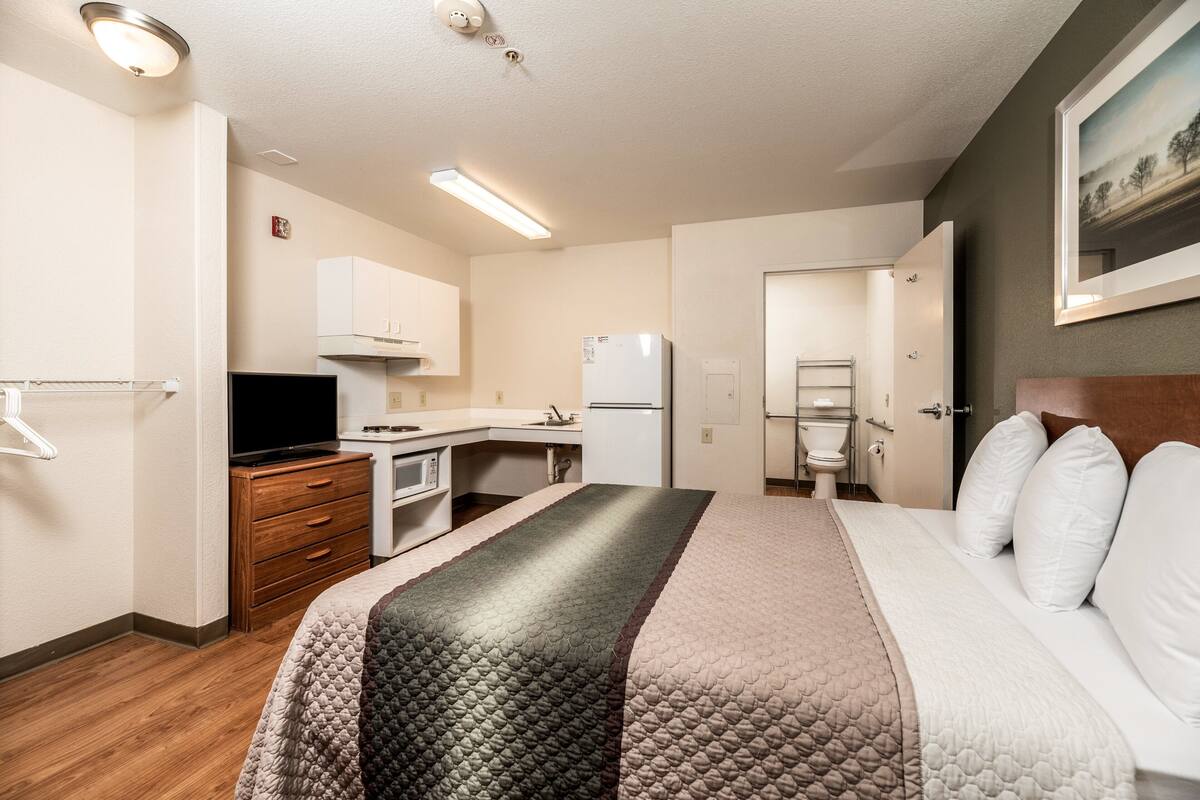 Habitación de hotel con cama, escritorio, refrigerador, microondas y televisión.