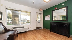 A hotel room with a large window, a door with an exit sign, a mirror, and a black cabinet. - HomeTowne Studios by Red Roof Fresno - West (Fresno)