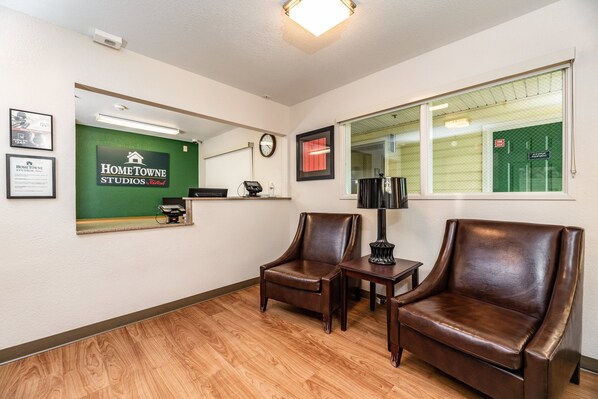 A reception area with a green sign, two leather chairs, a small table with a lamp, and a clock on the wall. - HomeTowne Studios by Red Roof Fresno - West (Fresno)