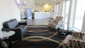 A hotel lobby with a reception desk, a sofa, two armchairs, a coffee table, and a patterned rug.