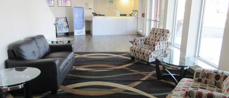 A hotel lobby with a reception desk, a sofa, two armchairs, a coffee table, and a patterned rug.