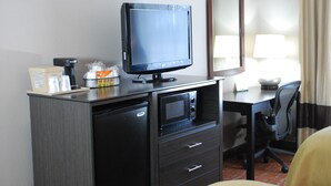 A compact hotel room with a kitchenette, a flat-screen TV, a microwave, a small refrigerator, a desk, and a chair.
