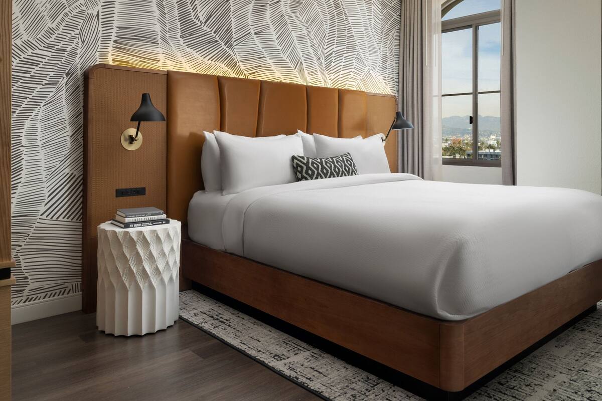 A modern bedroom with a large bed, a nightstand, a decorative vase, and a patterned wall.