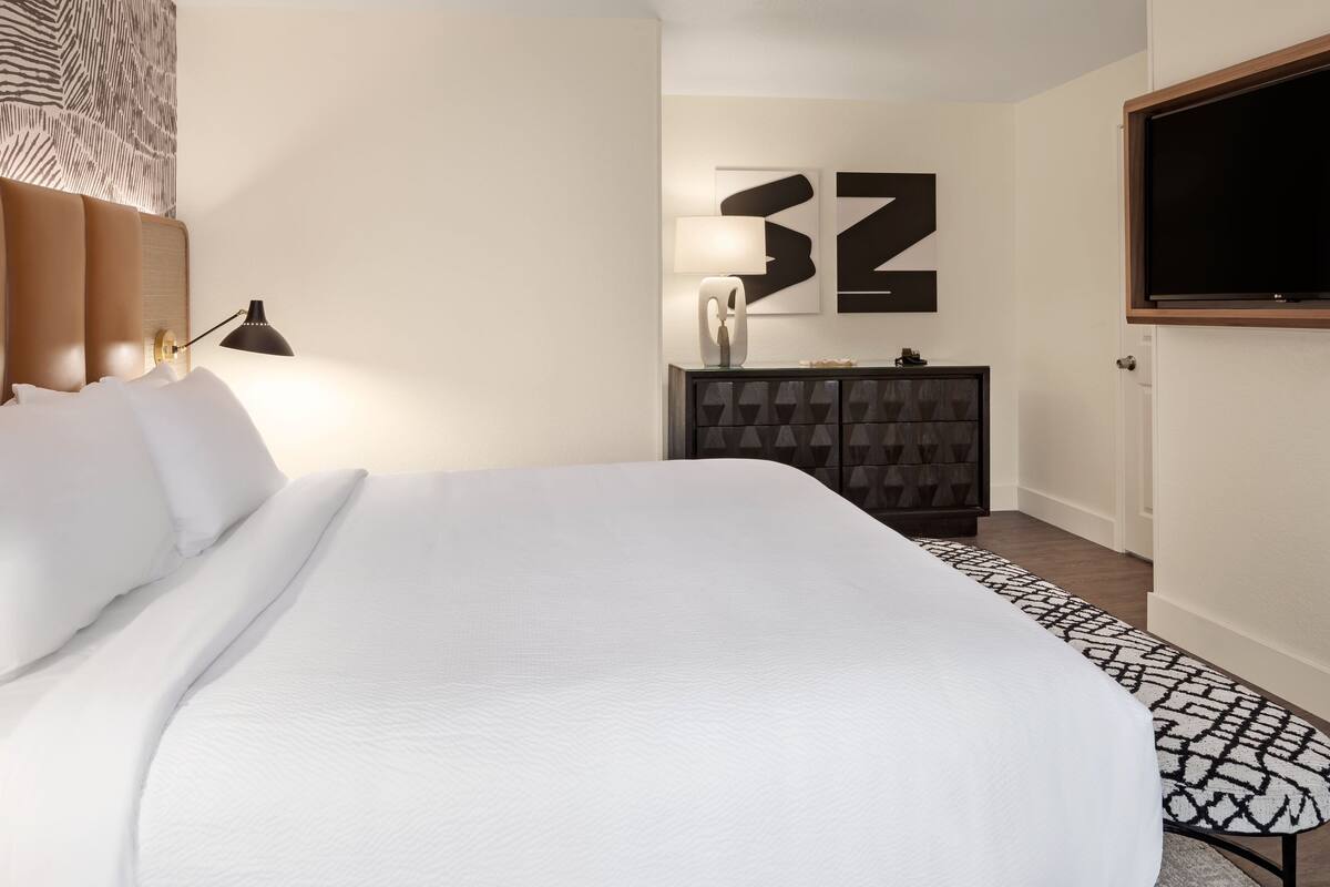 A modern hotel room with a large bed, a TV mounted on the wall, and a geometric-patterned cabinet.