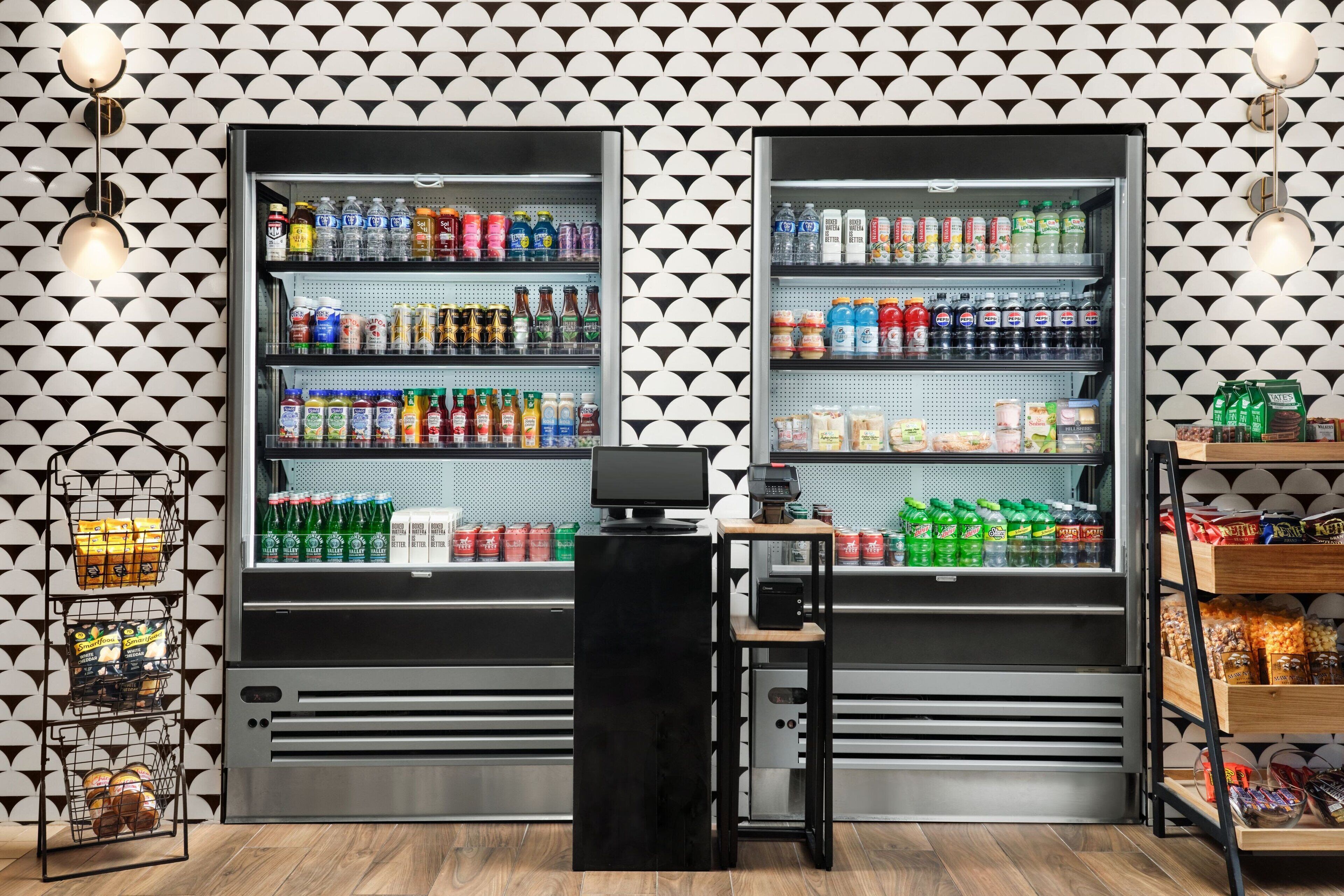 A refrigerated display case with various beverages and snacks, a payment terminal, and a patterned wall.