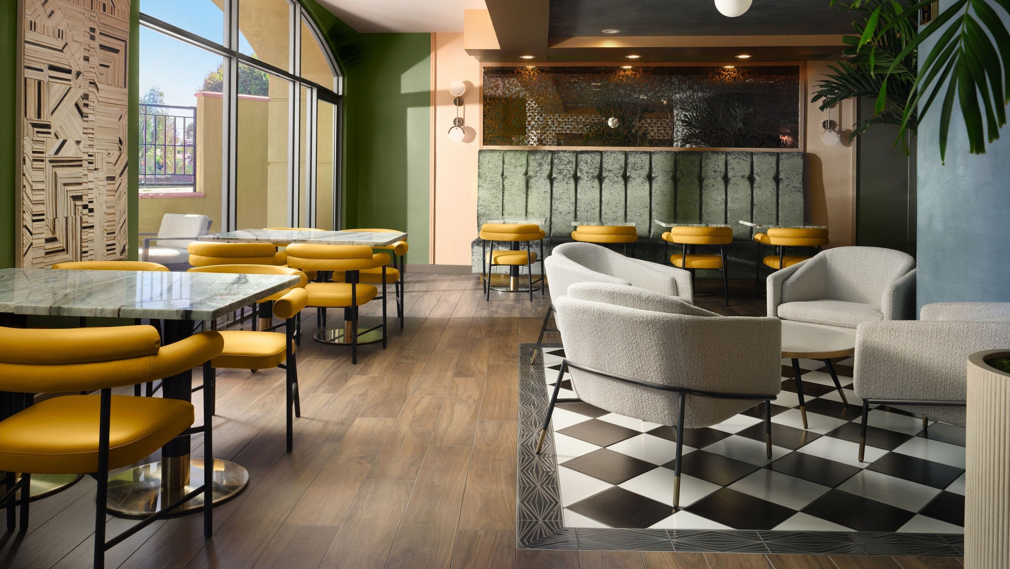 A modern restaurant interior with yellow and grey seating, a checkered floor, and a decorative wall.