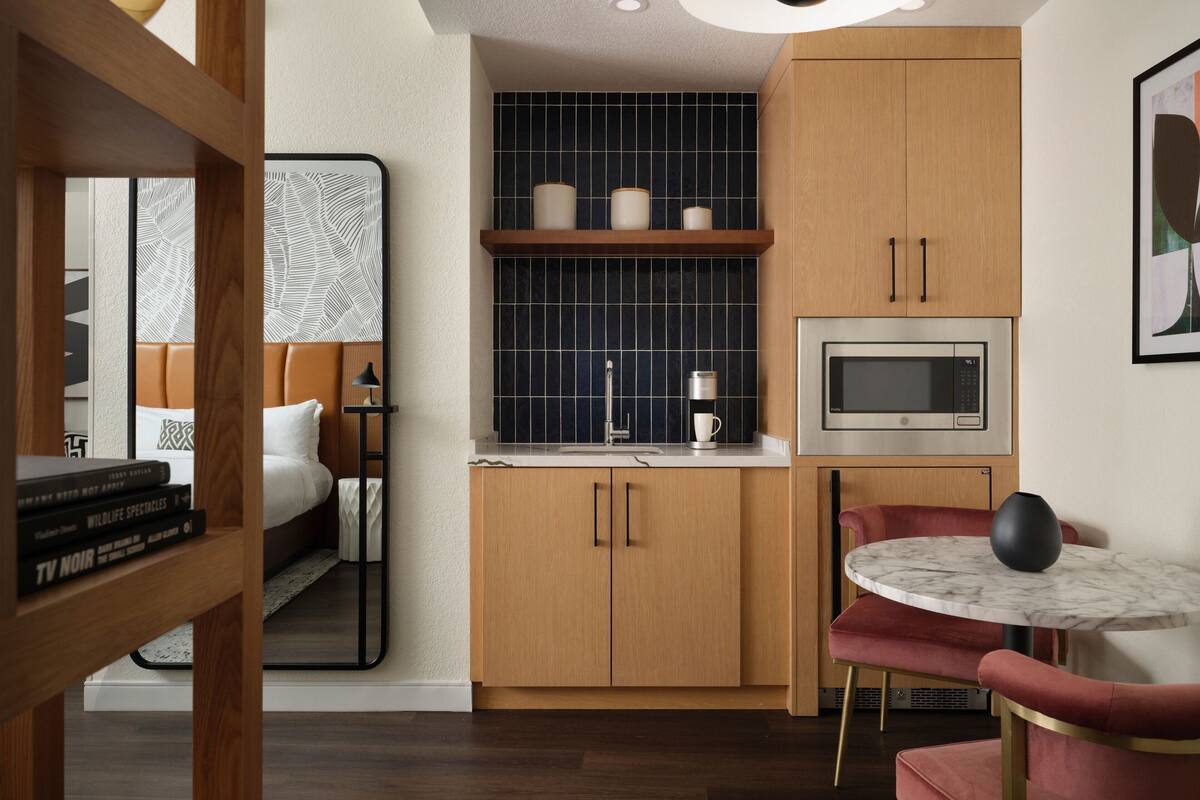A compact kitchen with wooden cabinets, a microwave, and a small dining area with a round table and red chairs.