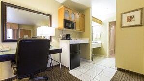 Een hotelkamer met een bureau, stoel, magnetron, koelkast en een badkamer die door een geopende deur zichtbaar is.