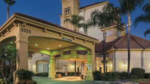 A hotel entrance with a covered area, palm trees, and a clear sky.