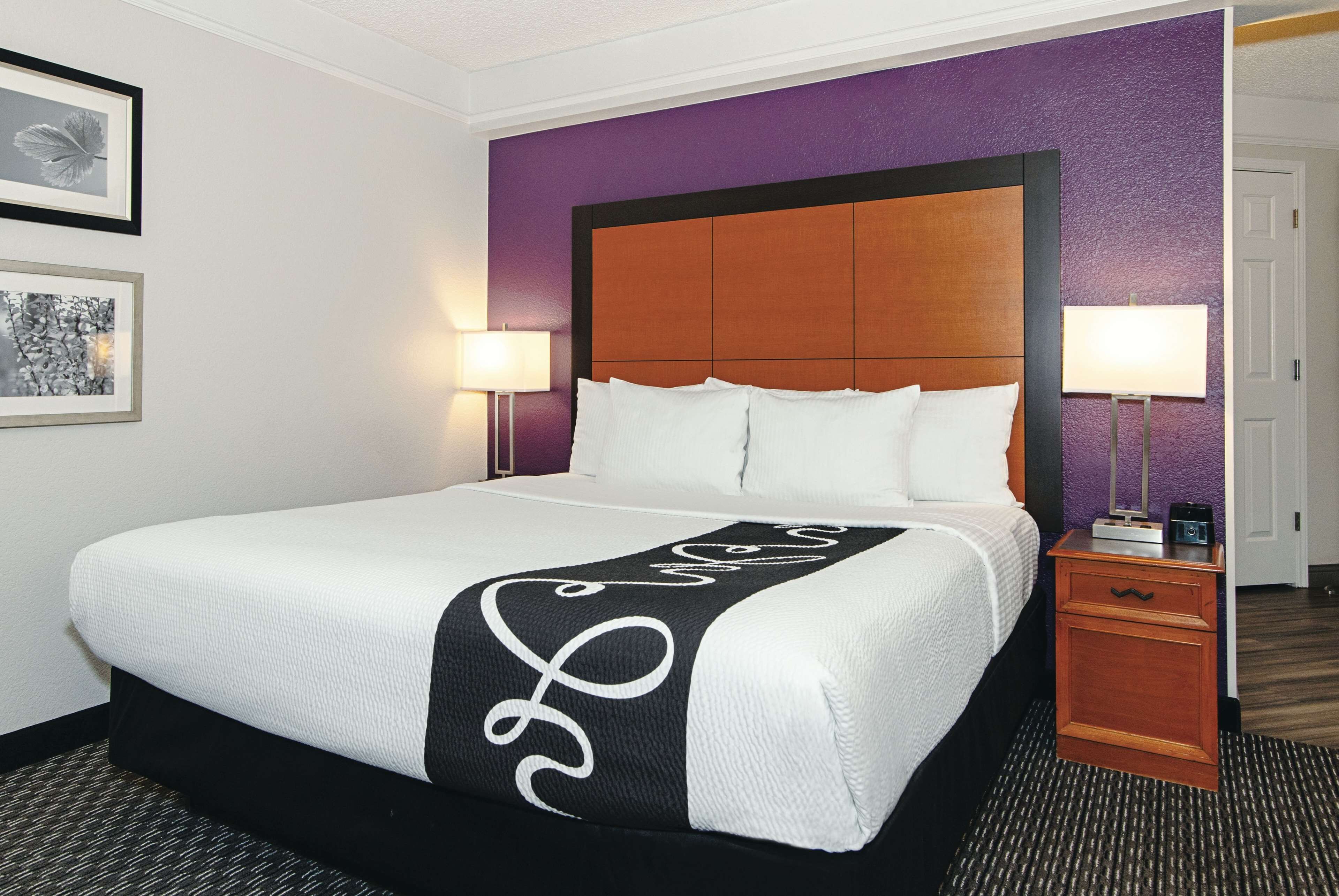 Una habitación de hotel con una cama grande, un cabecero de madera, dos lámparas de noche y una mesita de noche pequeña de madera.